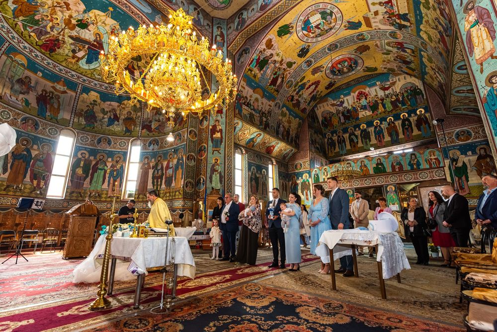 Orthodox church interior with ornate frescoes, chandelier, and guests gathered for a religious ceremony.