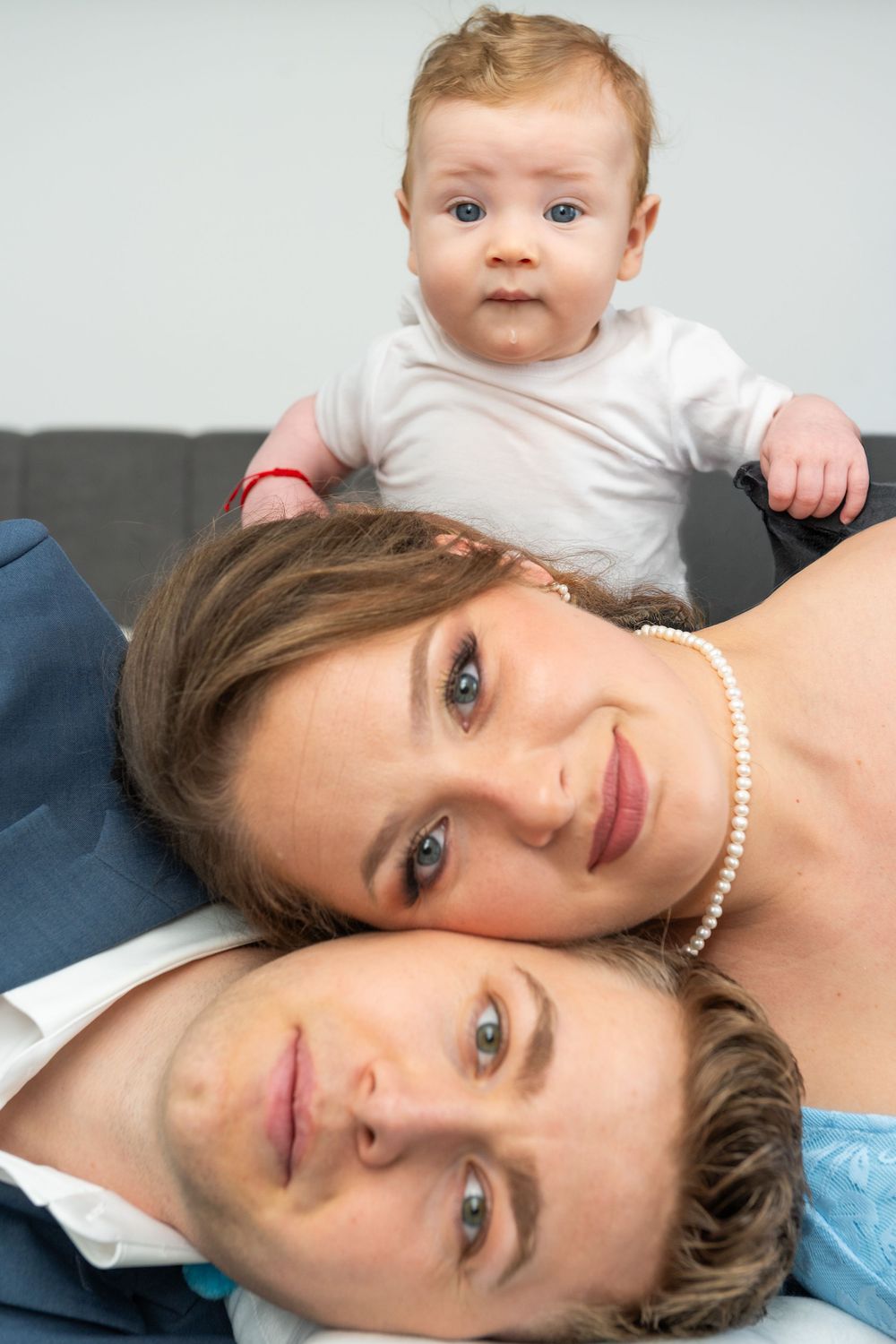 Young couple lying down with an adorable baby perched on top, smiling for a family portrait photo.