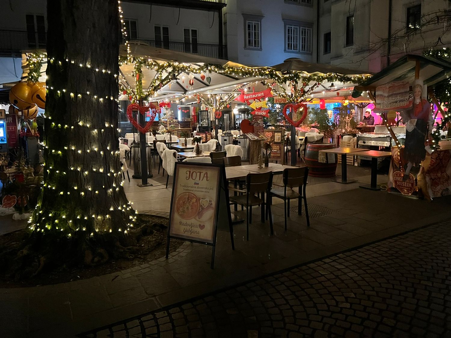Festive outdoor restaurant decorated with warm Christmas lights on a charming European cobblestone street at night.