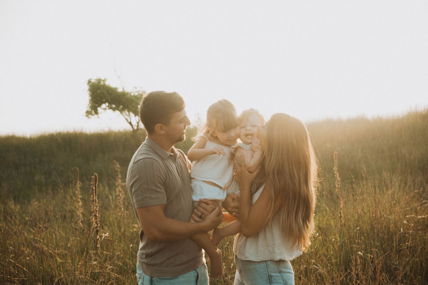 Family with young toddler sharing a tender moment in a sunlit golden field at sunset.