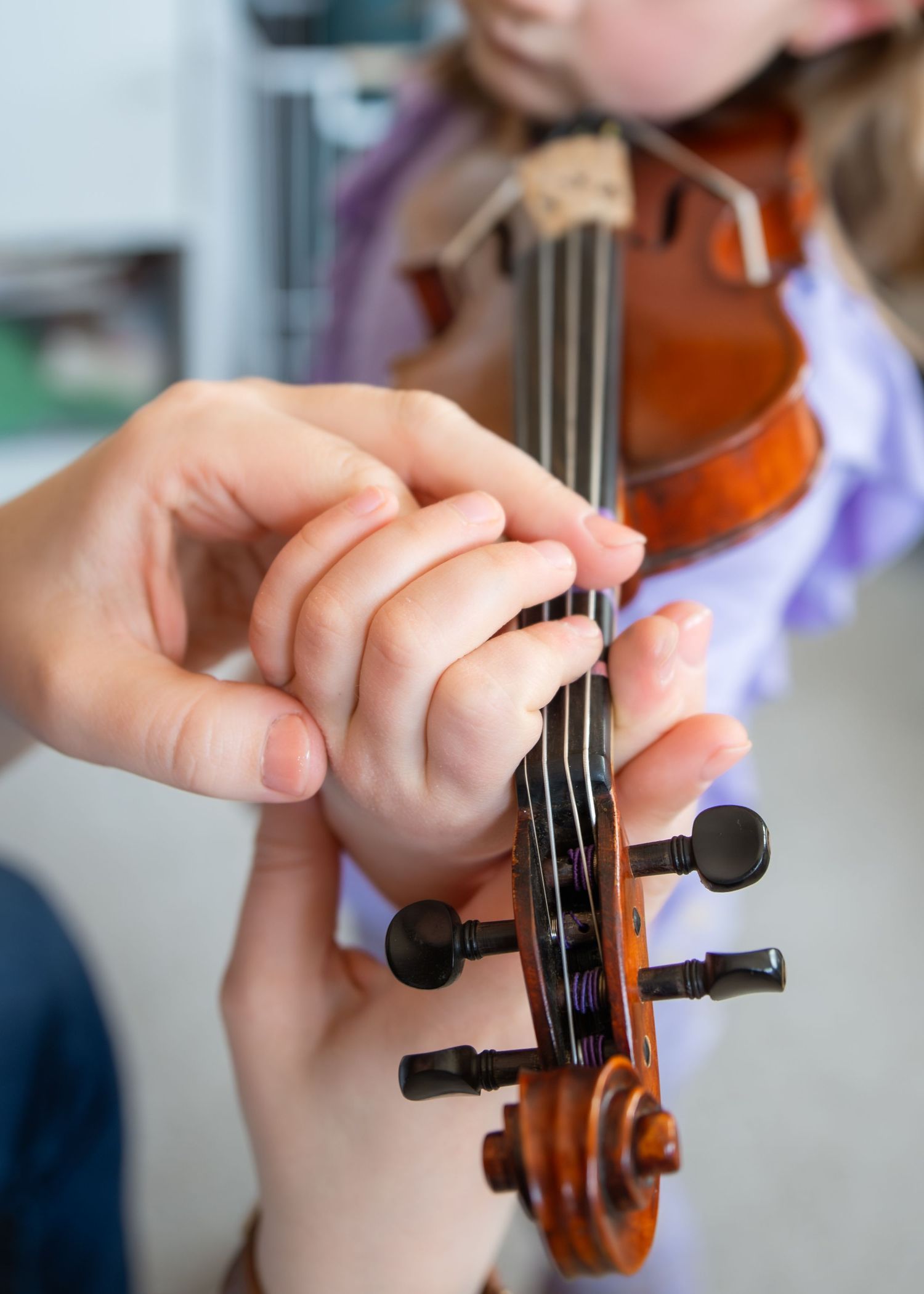 A teacher guides a young child's fingers on a violin fingerboard during a music lesson.