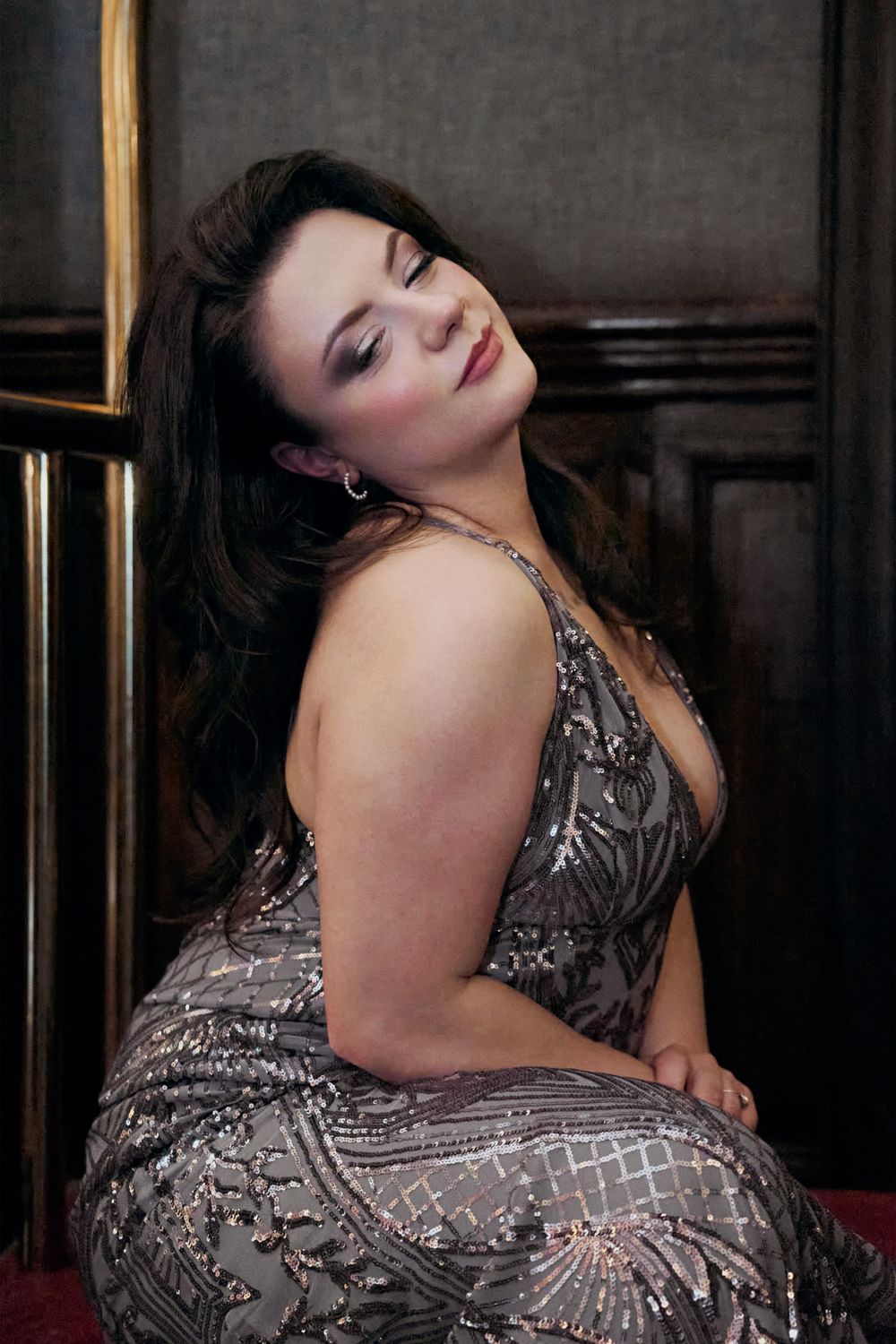 A glamorous woman in a silver sequined gown poses elegantly with dark wavy hair and smoky eye makeup.