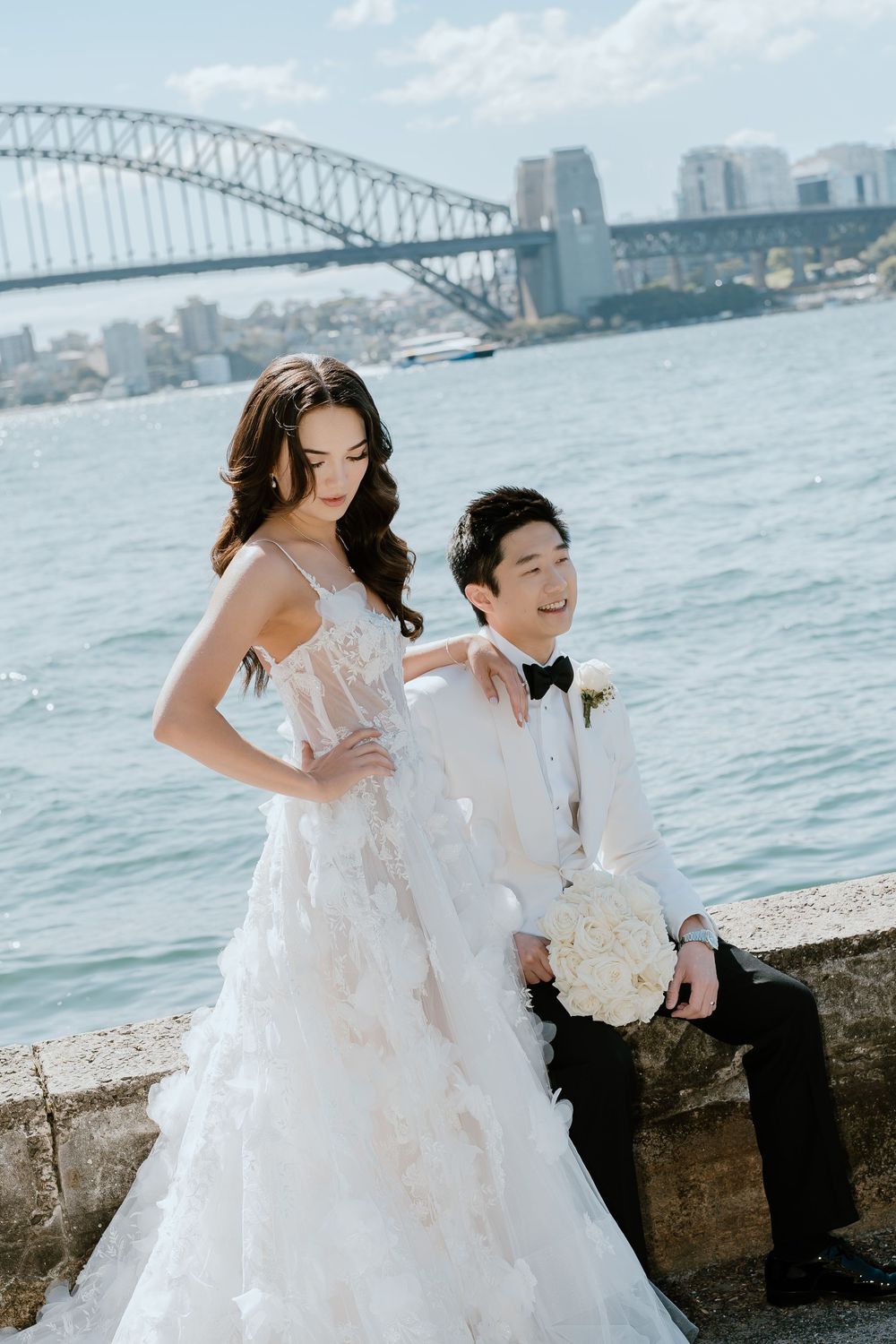 Bride and groom posing by Sydney Harbour with the iconic Harbour Bridge backdrop on their wedding day.