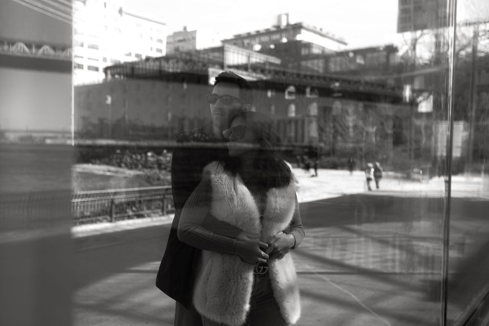 Black and white reflection photo of couple embracing near glass window in urban setting.