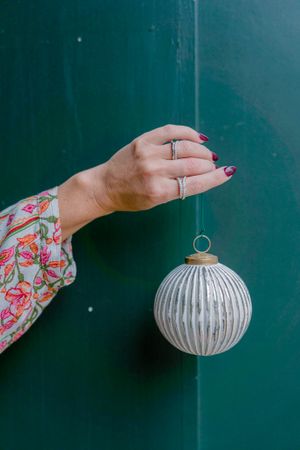 Hand wearing rings reaching towards vintage white striped Christmas ornament.