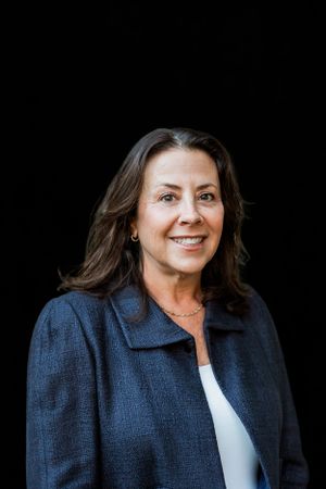 Professional portrait of woman in navy blazer against black background.