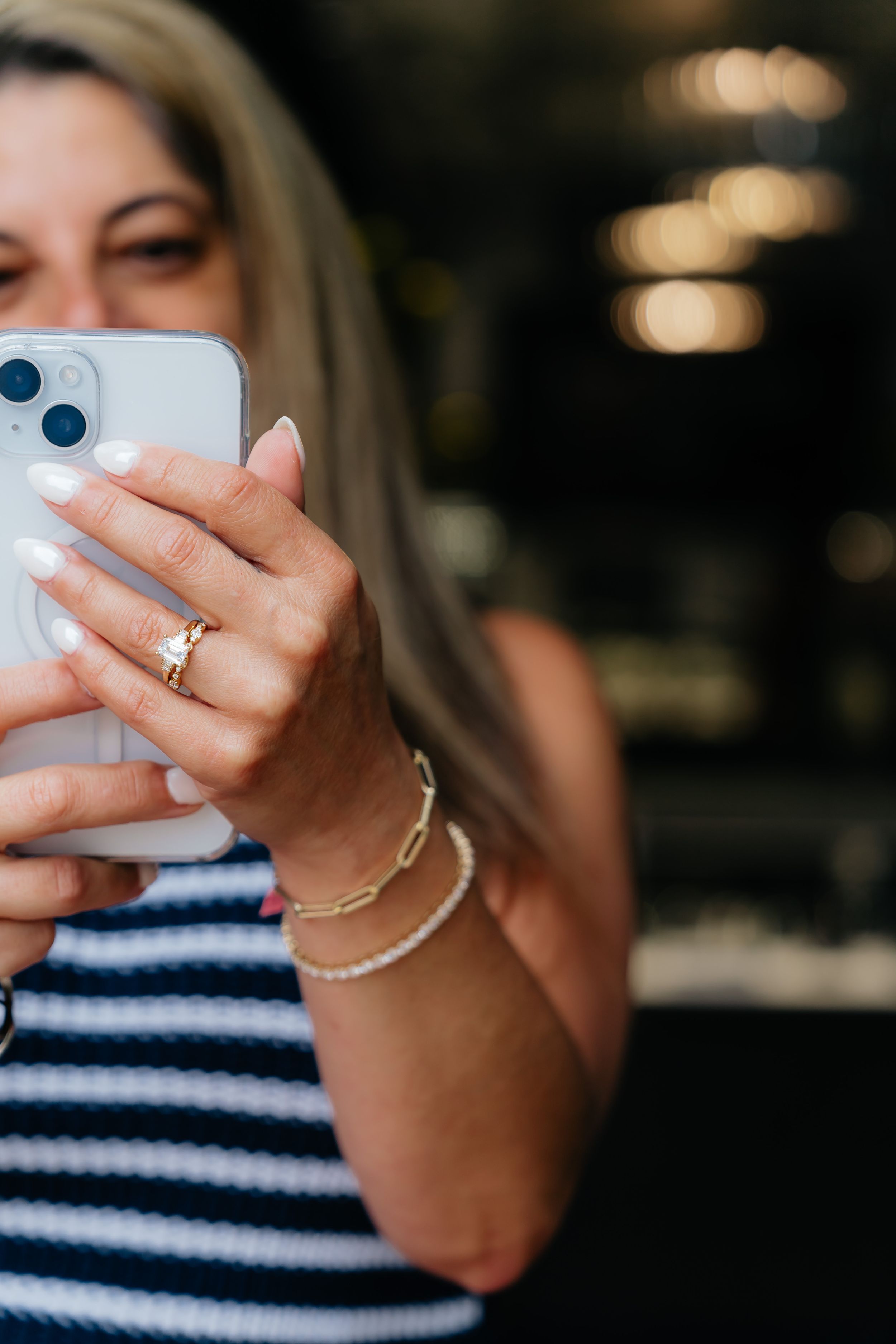 Hand holding iPhone showing engagement ring and layered bracelets.