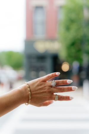 Hand displaying elegant diamond rings and gold chain bracelet against urban background.