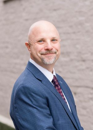 Professional headshot showing a person in business attire smiling against a gray background.