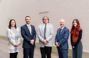 Group of five professionals standing together against a wall in business attire.