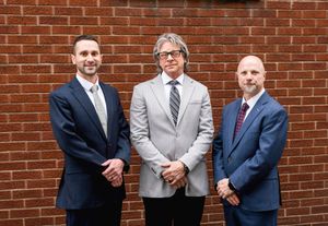 Three professionals in suits stand together against a brick wall background.