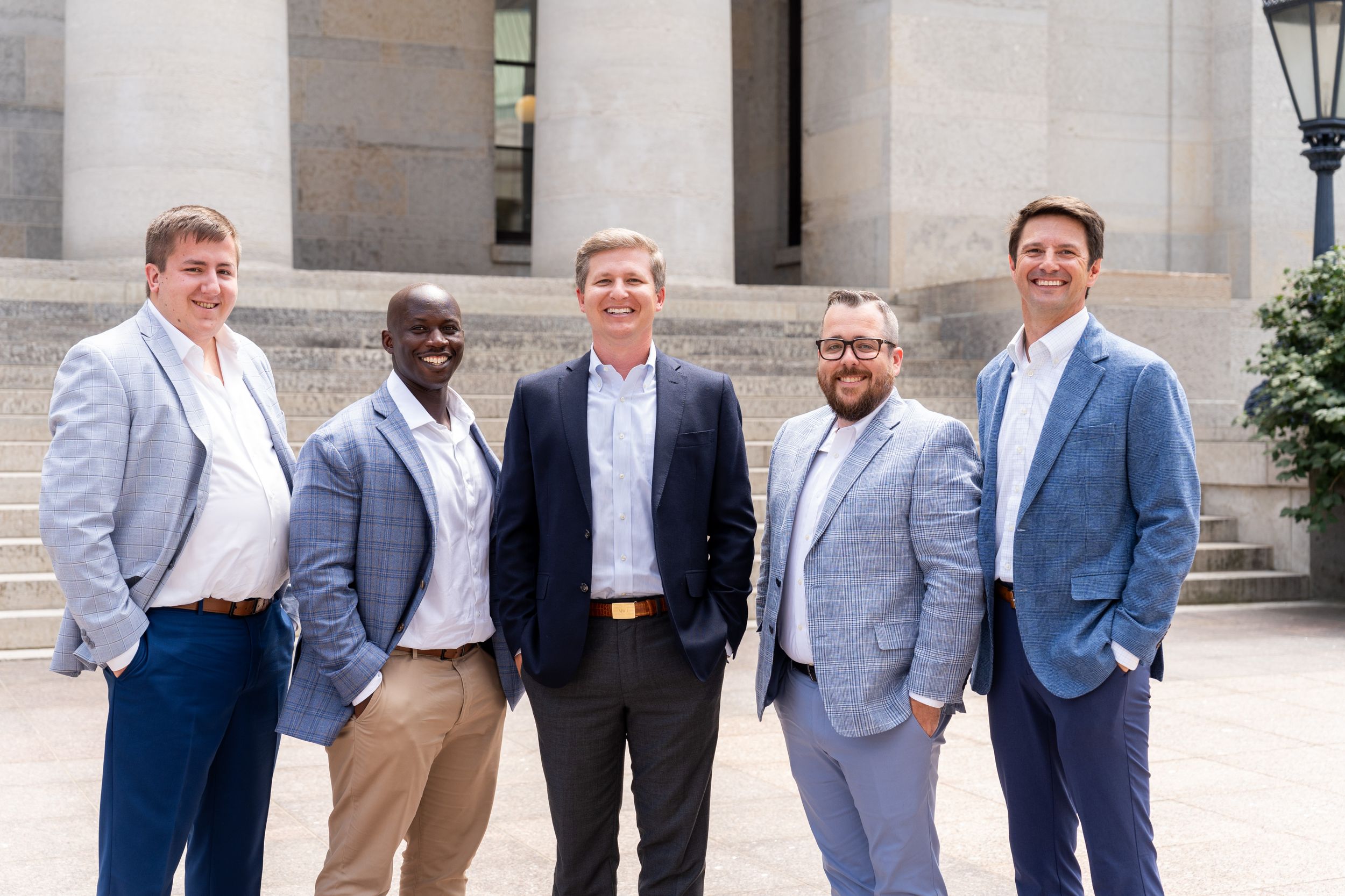 Professional group photo of five people in business attire standing in front of classical columns.