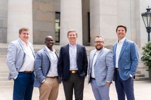 Business team of five people posed formally in front of a building with columns.