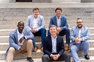 Group of five professionals in business attire seated and standing on stone steps.