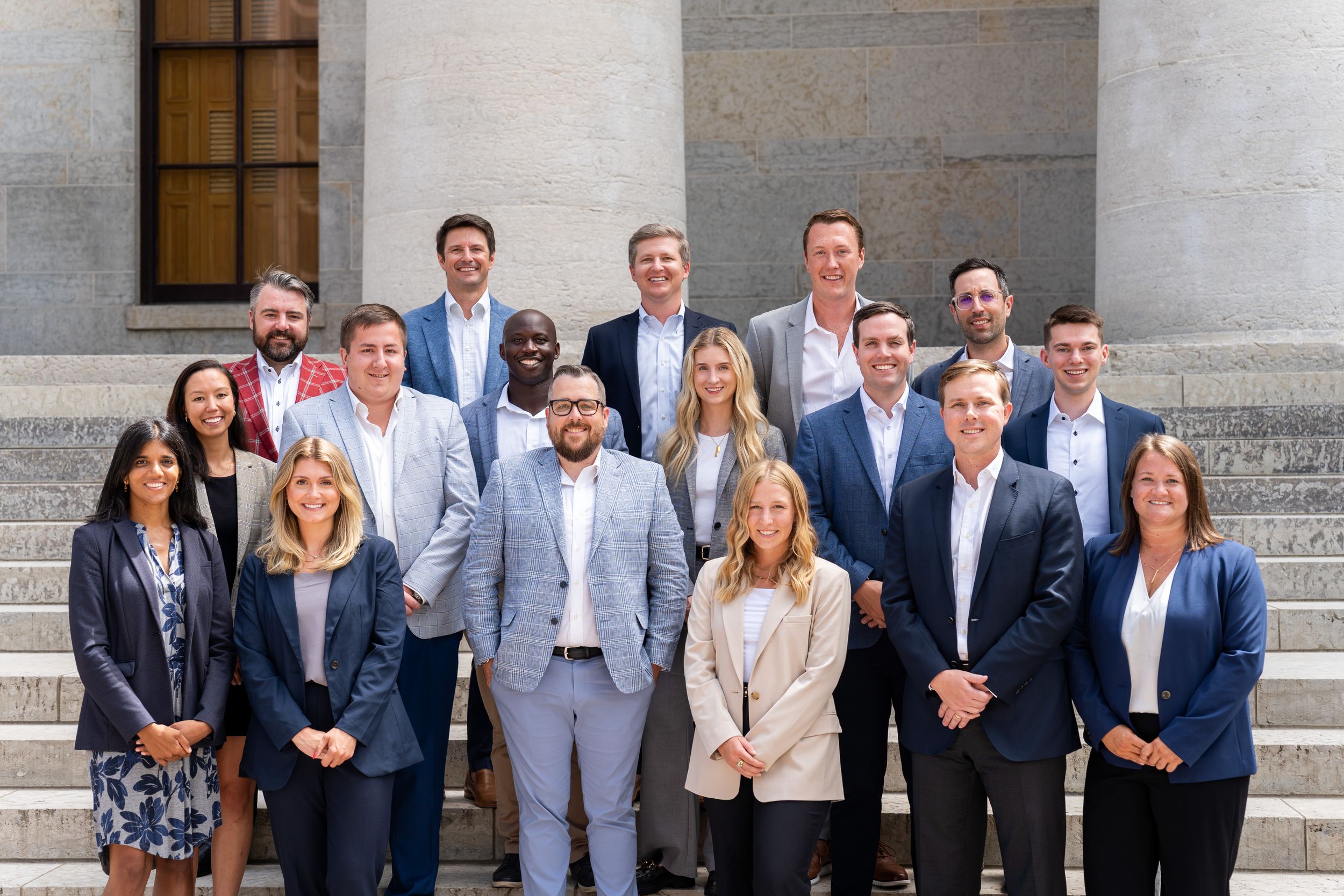 Professional business team poses for group photo on concrete steps of building with columns.
