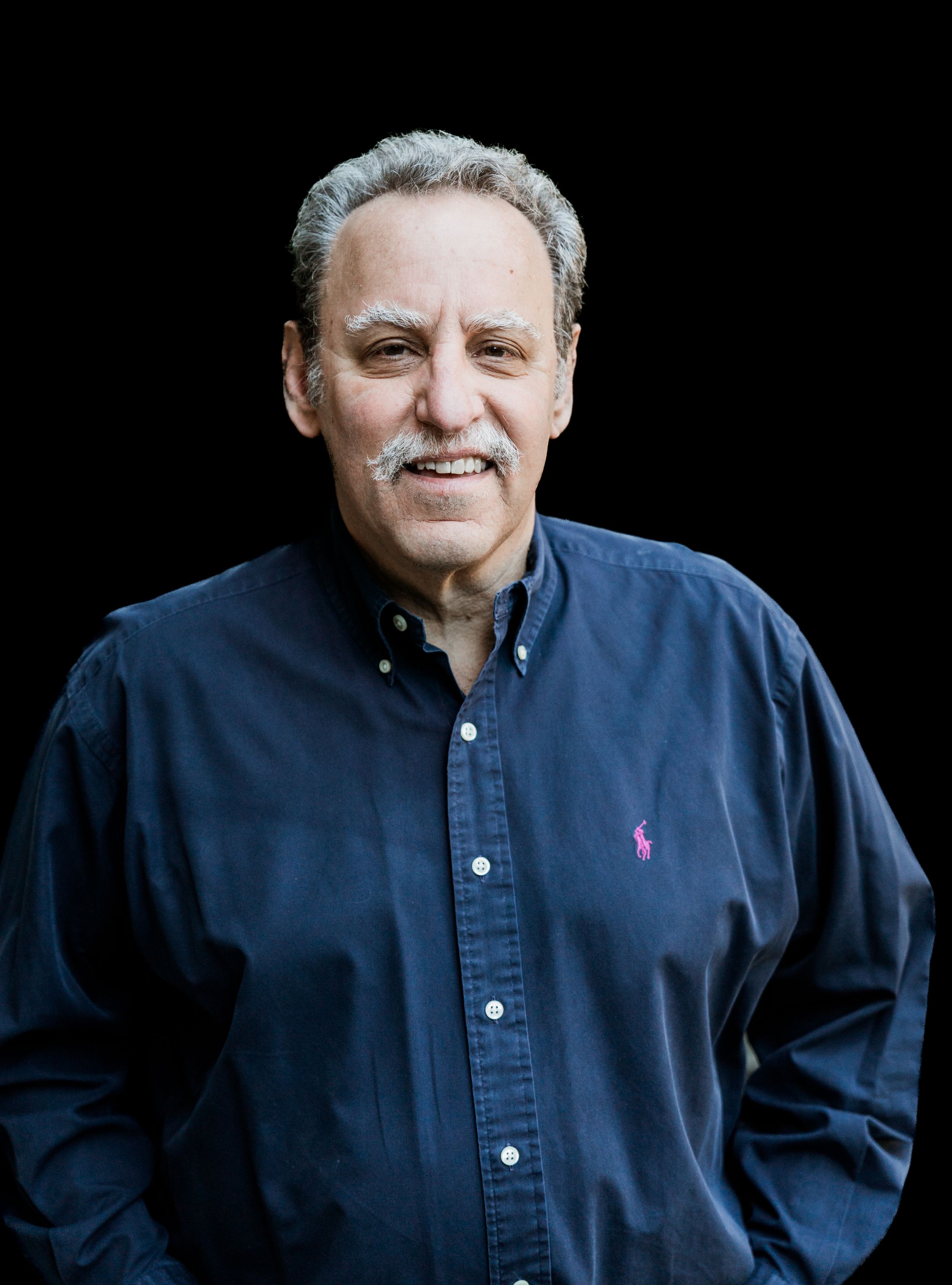 Professional headshot of man in blue button-down shirt against dark background.