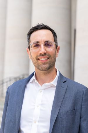 Professional wearing glasses and blue blazer smiles in front of architectural columns.