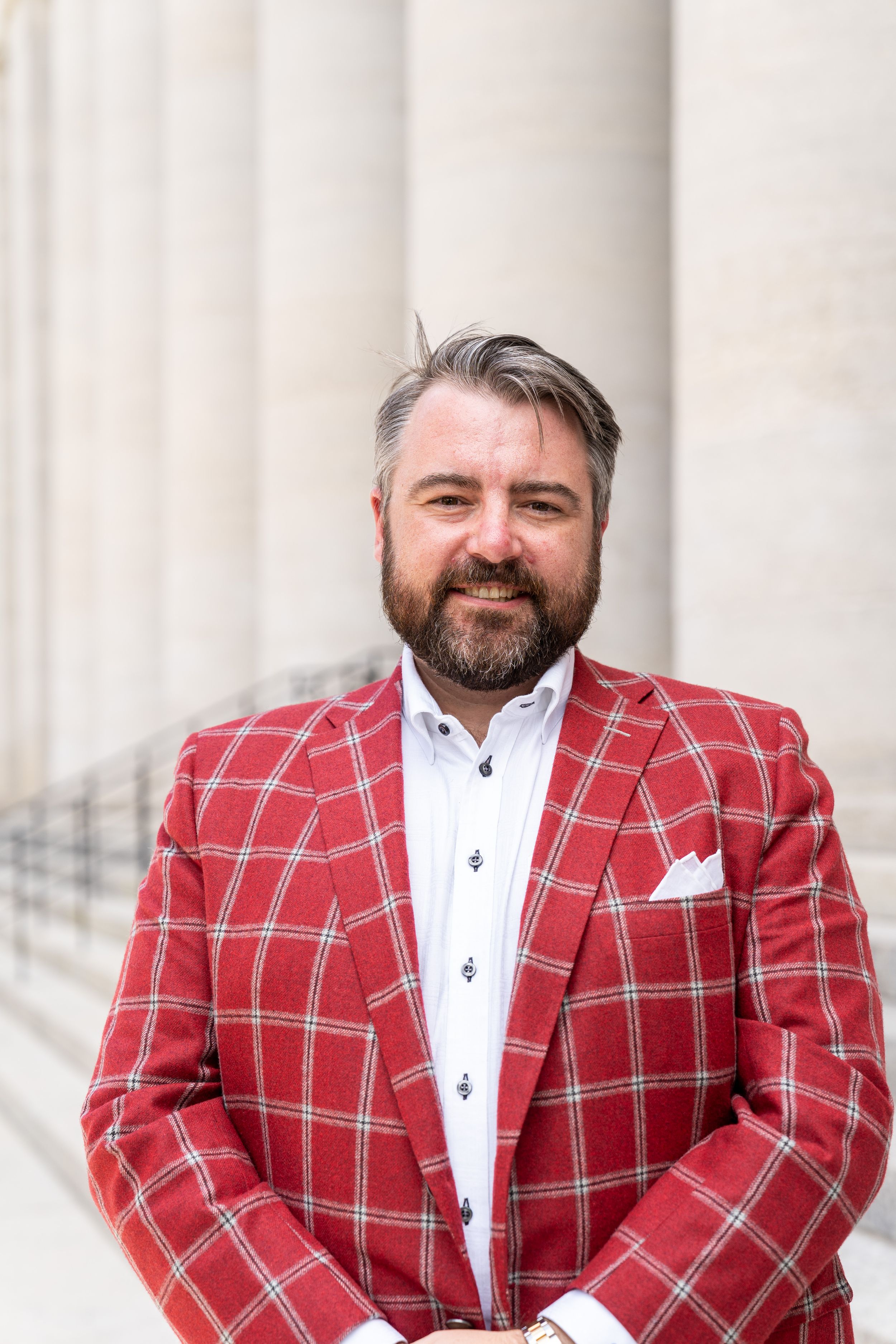 Person wearing red plaid blazer and white shirt poses in front of stone columns.