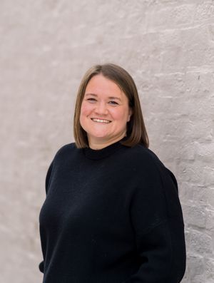 Person smiling while wearing a black sweater against a light gray wall.