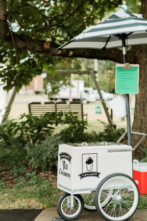 Vintage ice cream cart with striped umbrella and menu board in garden setting.