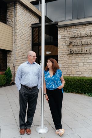 Two colleagues conversing by a flagpole outside a modern office building entrance.