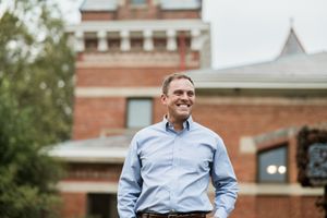 Political candidate in light blue button-down shirt standing outdoors.