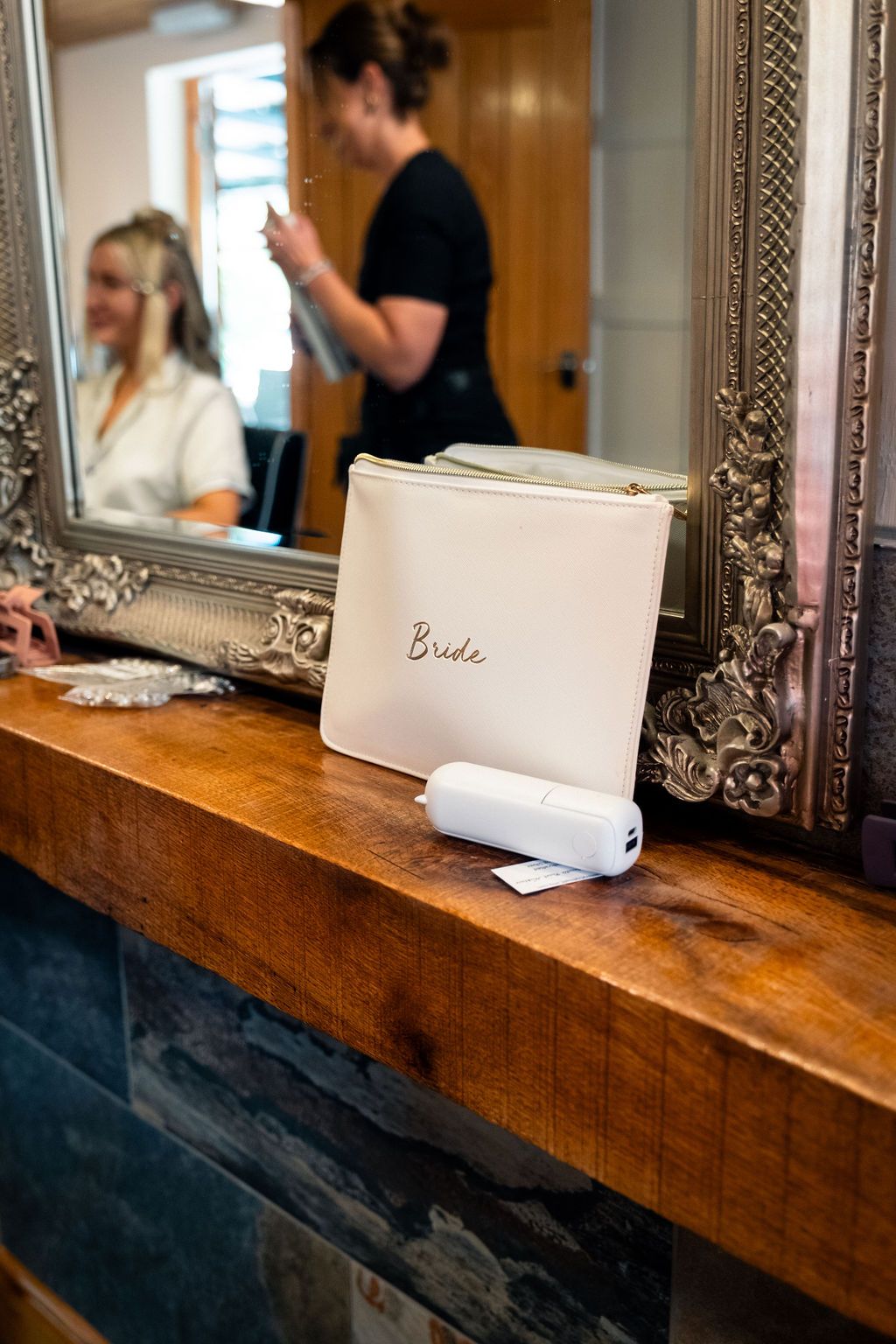 Bridal pouch labeled "Bride" and a portable device sitting on a wooden shelf in front of a mirror, with bride reflection