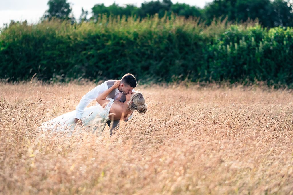 Bride and groom sharing a kiss in a sunlit field at Coton House Farm wedding venue.