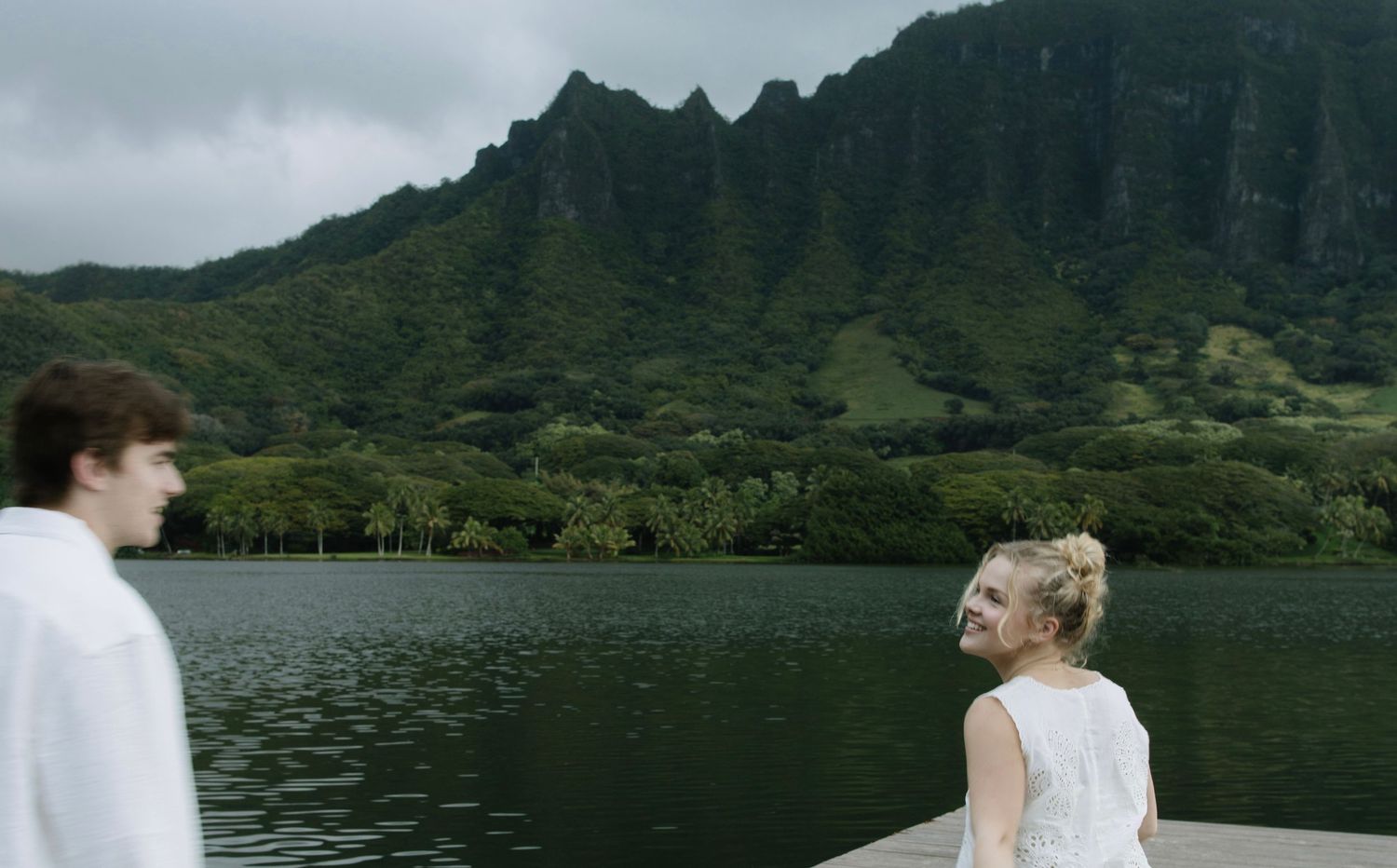 Two people looking out at scenic mountain lake view in overcast weather.