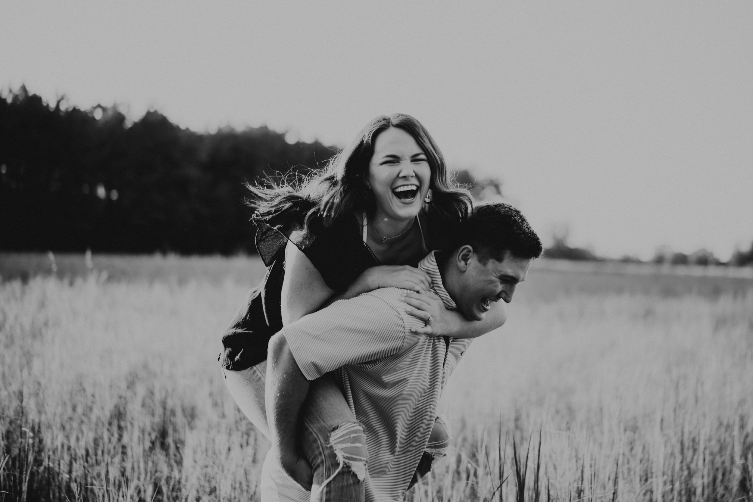 A black and white still of a girl laughing freely while being carried by her fiance.