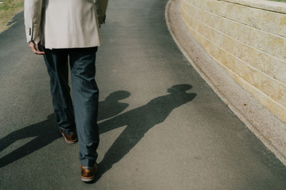 Shadows cast on a curved pathway show a person walking in formal attire.