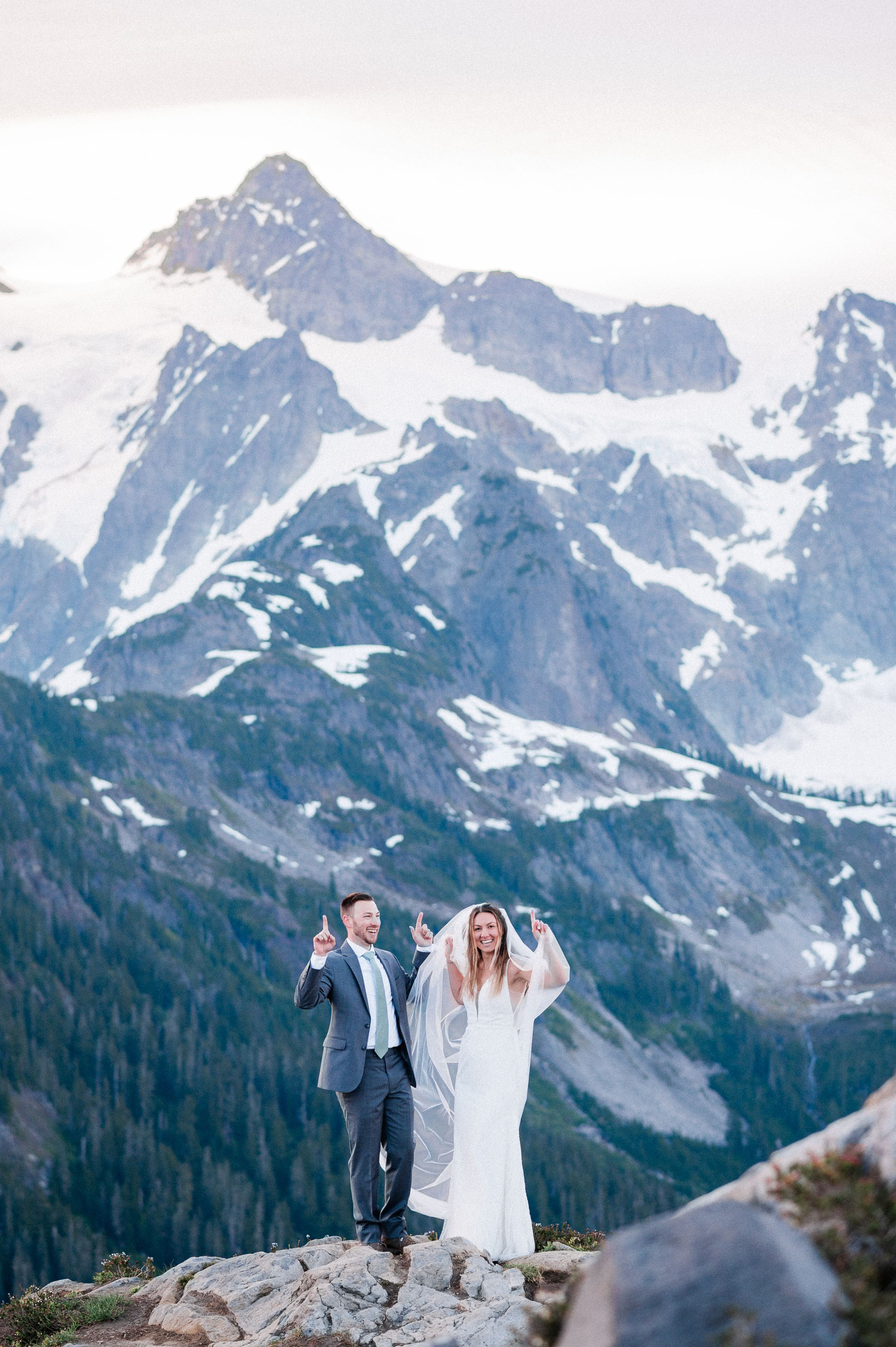 bride and groom dancing on top of mountain with blue snow capped mountains behind them during their Washington Elopement.