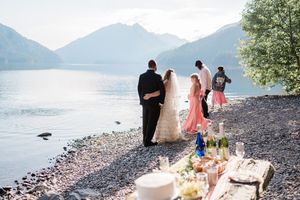 bride and groom looking out at lake while children throw rocks into the water.