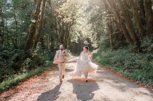 bride and groom running down forest road with light shining behind them