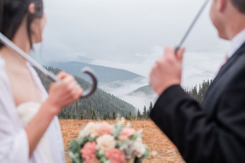 bride and groom out of focused while holding umbrellas with the foggy mountains revealing themselves in background.