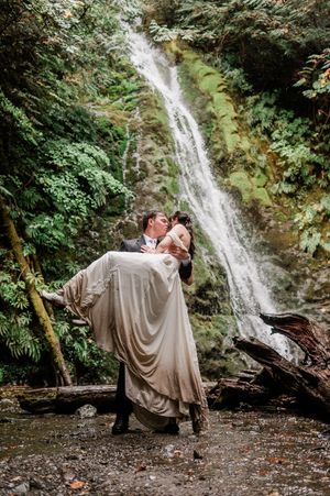 groom holding bride while kissing in front of moody waterfall