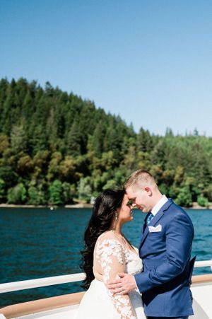 A romantic wedding couple embraces on the Lady Alderbrook with evergreen forest and blue lake waters in the background.