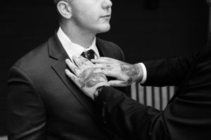 A black and white wedding photo showing a close up a groomsmen with tattoos on hands fixing grooms tie