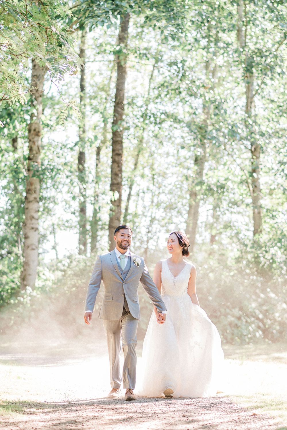 bride and groom walk hand in hand on dusty road with sunlight shinning behind them