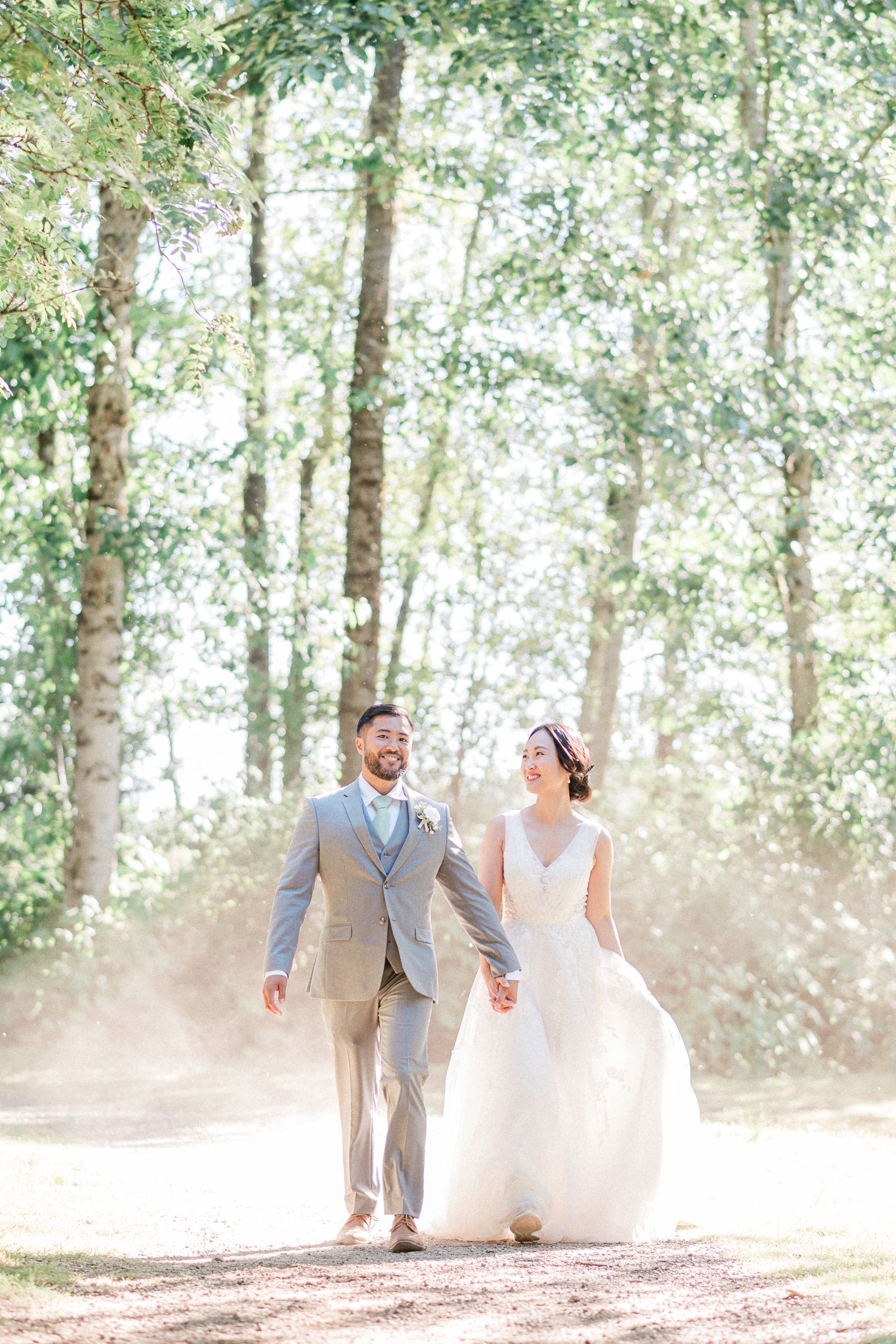 bride and groom walk hand in hand on dusty road with sunlight shinning behind them