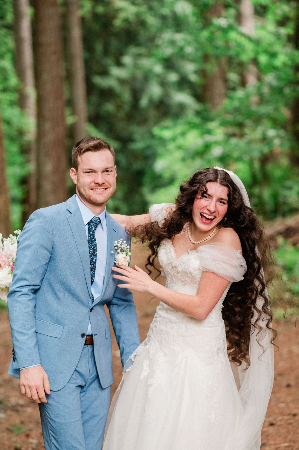 A happy couple shares joyful candid moments in a wooded outdoor setting during their wedding day