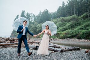 A couple celebrates their wedding on a misty Pacific Northwest beach with evergreen trees in the background.