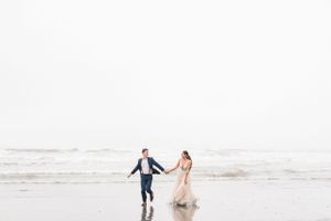 A couple in wedding attire walks along the misty Ruby Beach shoreline in Olympic National Park during an overcast day