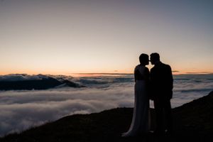 Silhouetted couple embraces against dramatic sunset sky with mountains and fog rolling in the background.