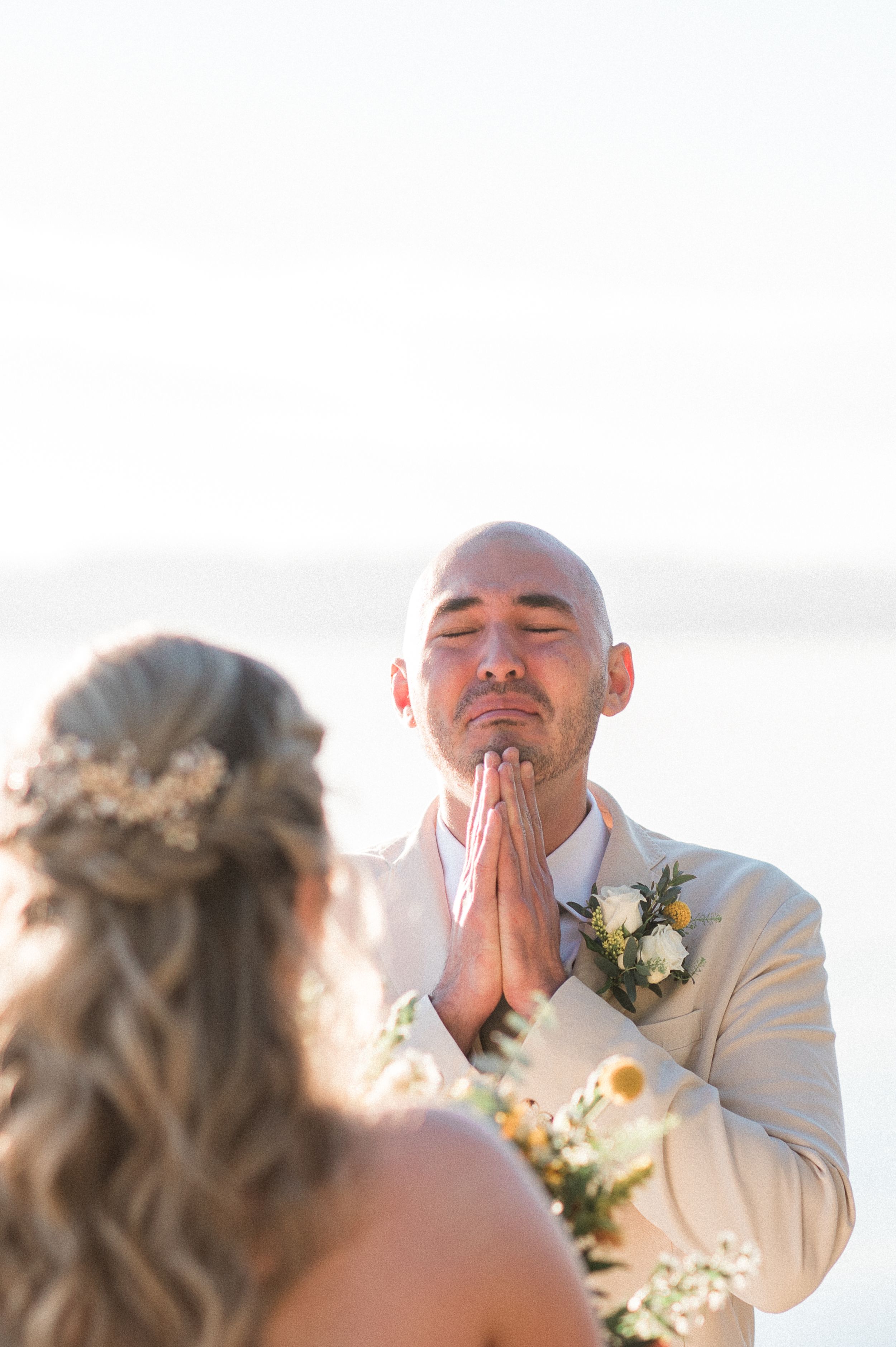 A groom in a white suit jacket shows an emotional reaction during a wedding ceremony.