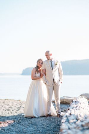 A couple in wedding attire poses at Owen Beach with mountains and water in the background.
