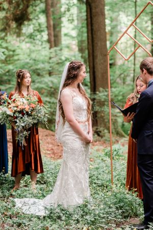 A couple shares vows in a lush forest setting with copper-colored geometric wedding decor.