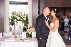 A newlywed couple shares a romantic kiss beside an elegant floral arrangement and reception table.