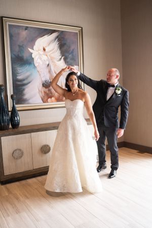 A couple in wedding attire dance and twirl beneath a striking white horse painting in an elegant indoor setting at The Club at Arrowcreek.