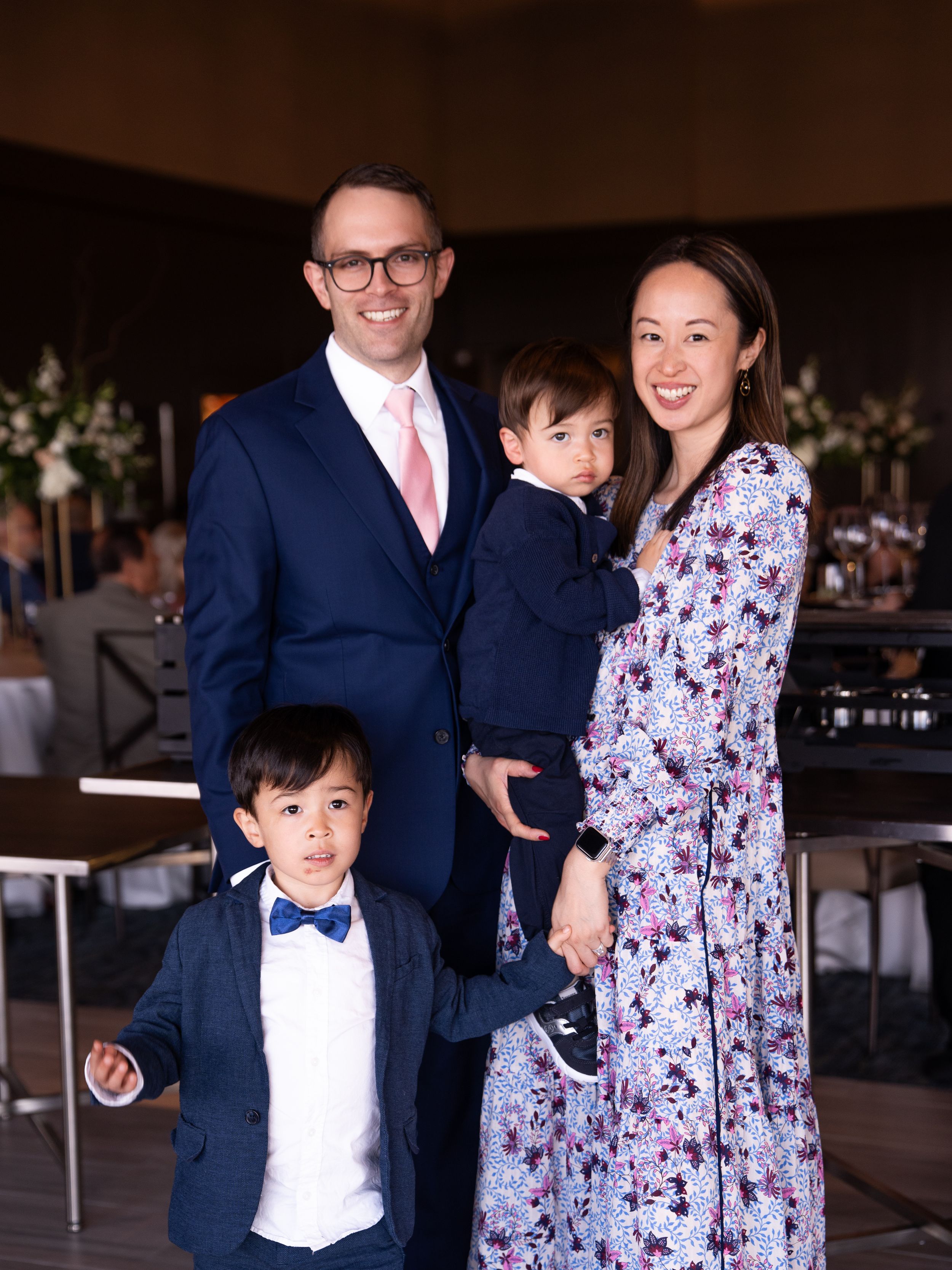 A family of four poses together at a wedding at The Club at Arrowcreek, wearing coordinated navy blue and pink outfits.